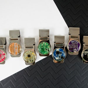 May include: Seven silver money clips with different coloured circuit board designs. The designs include red, orange, green, blue, purple, and black.