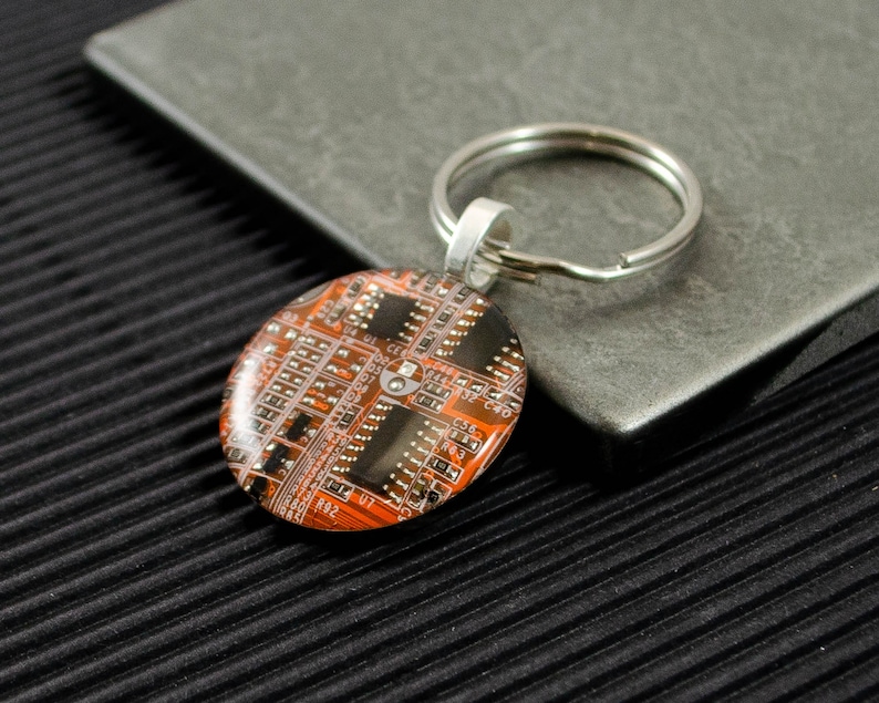May include: A silver key chain with a round orange and black circuit board design charm.