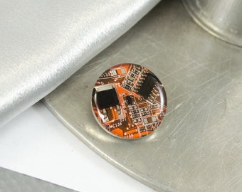 May include: A round, orange and black, epoxy resin pin with a circuit board design. The pin features text including "C138" and "D196".
