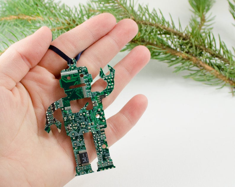 Pode incluir: Um ornamento de rob&ocirc; de placa de circuito verde com um cord&atilde;o preto para pendurar.