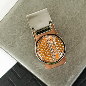 May include: A silver money clip with a round, clear, orange-colored resin insert featuring a circuit board design.