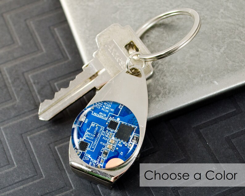 May include: A silver key ring with a blue and silver round charm featuring a circuit board design. The text "Choose a Color" is visible below the charm.
