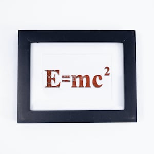 May include: A framed print featuring the equation E=mc². The text is in a reddish-brown color and set against a white background. The frame is black and rectangular.