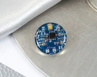 May include: A round, blue epoxy resin keychain featuring a circuit board with various electronic components and text, including "R248", "R245", "C306", "R317", "C321", "C29", "C288", "C327", and "R302".
