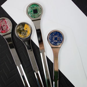 K&ouml;nnte beinhalten: Vier silberne Brief&ouml;ffner mit verschiedenen farbigen Platinen-Designs. Die Platinen sind rot, gelb, gr&uuml;n und blau.