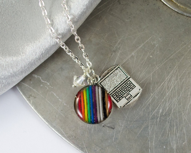 May include: A silver chain necklace with a rainbow striped charm, a silver laptop charm, and a clear crystal charm.