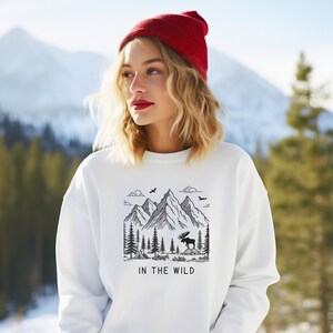 May include: White sweatshirt with a black and white graphic of mountains, trees, and a moose. The text "IN THE WILD" is printed below the graphic.