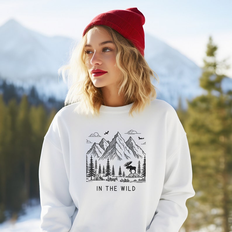 May include: White sweatshirt with a black and white graphic of mountains, trees, and a moose. The text "IN THE WILD" is printed below the graphic.