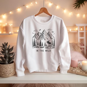 May include: White sweatshirt with a black graphic of a mountain range, a moose, and trees. The text "IN THE WILD" is printed below the graphic.
