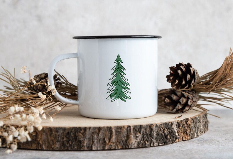 K&ouml;nnte beinhalten: Eine wei&szlig;e Emailletasse mit schwarzem Rand und einem gr&uuml;nen Tannenbaum-Design.