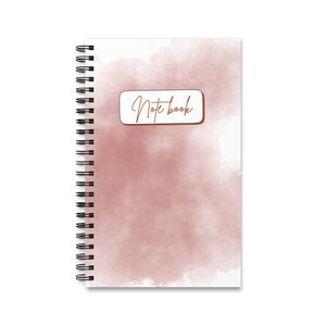Peut inclure: Un cahier à spirales avec un motif de style aquarelle. La couverture présente un lavis rose tendre avec les mots "Note book" dans une police manuscrite. Le cahier a un fond blanc.