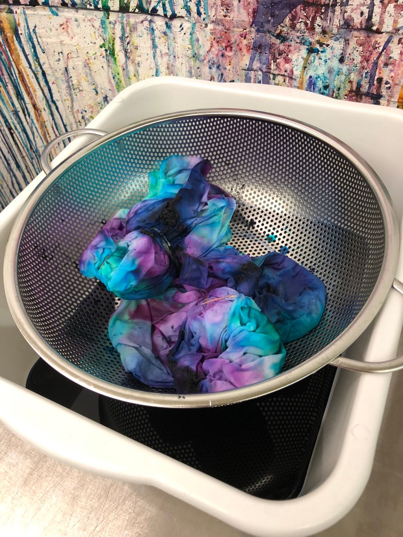 May include: A white plastic tub with a stainless steel colander inside. The colander contains a tie-dye fabric in shades of blue, purple, and black.