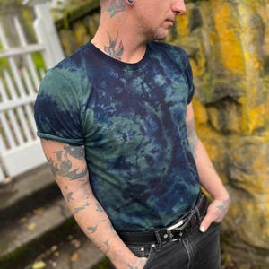 May include: A tie-dye t-shirt in shades of green and blue with a swirling pattern. The shirt has short sleeves and a crew neck.