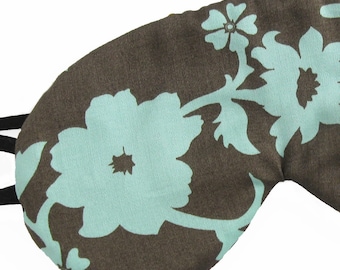 May include: A brown sleep mask with a light blue floral pattern. The mask has a black elastic strap.