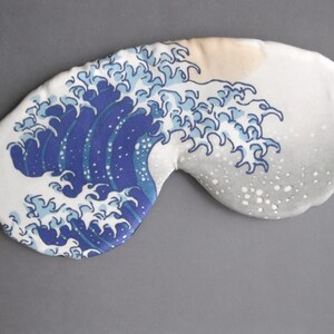 May include: A white sleep mask with a blue and white wave pattern. The wave pattern is reminiscent of the Great Wave off Kanagawa by Hokusai.