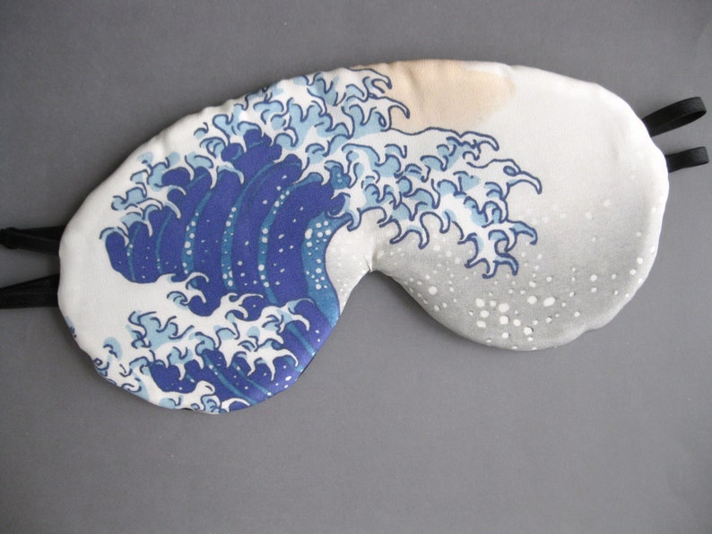 May include: A white sleep mask with a blue and white wave pattern. The wave pattern is reminiscent of the Great Wave off Kanagawa by Hokusai.