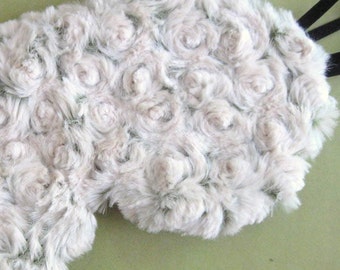 May include: A white sleep mask with a rose pattern. The mask is made of soft, fluffy fabric and has an elastic strap.