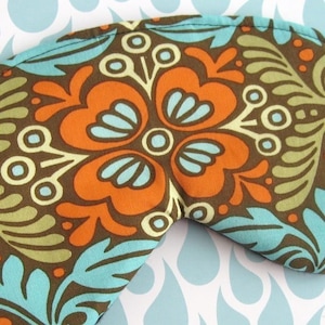 Könnte beinhalten: Eine braune Schlafmaske mit einem floralen Muster in Orange-, Blau- und Grüntönen. Das Muster zeigt stilisierte Blumen und Blätter.