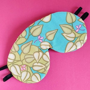 May include: A turquoise blue sleep mask with a floral pattern of green and white leaves. The mask has black elastic straps.