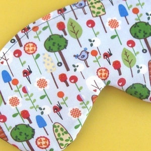 May include: A blue sleep mask with a whimsical pattern of trees, flowers, birds, and ladybugs. The pattern is in shades of red, green, yellow, and white.