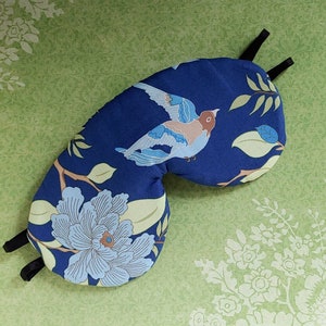 May include: Blue sleep mask with a floral and bird design. The mask has a dark blue background with a white bird and flowers in shades of pink, green, and yellow.