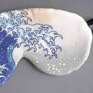 May include: A white sleep mask with a blue and white wave design. The wave design is reminiscent of the Great Wave off Kanagawa by Hokusai.