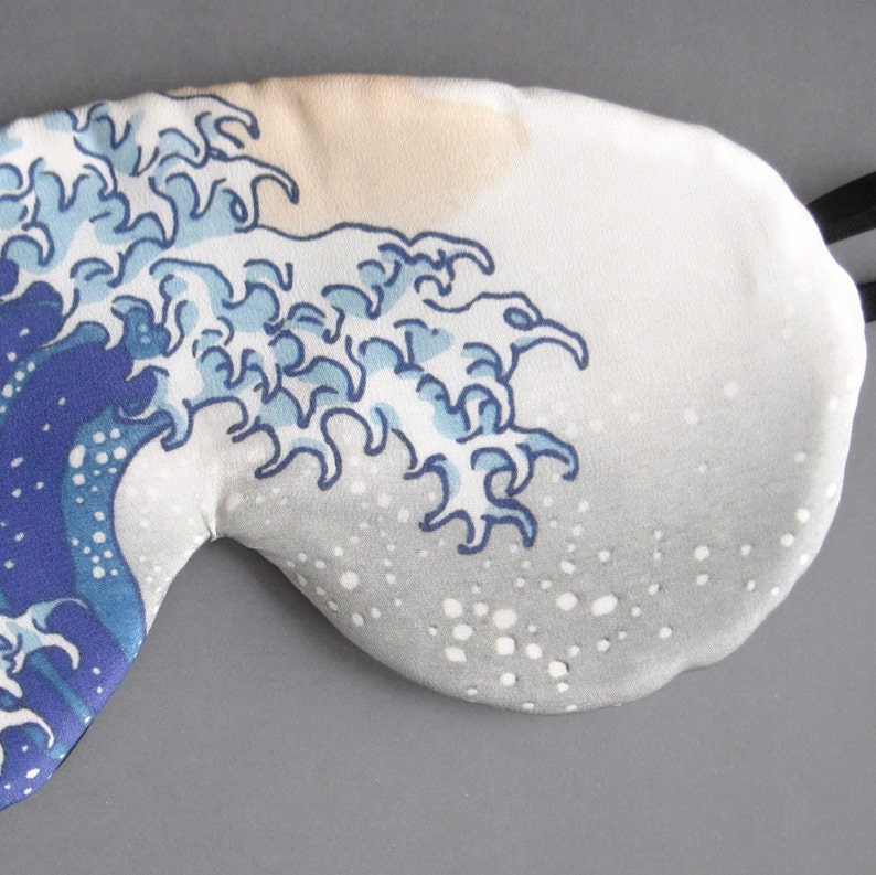 May include: A white sleep mask with a blue and white wave design. The wave design is reminiscent of the Great Wave off Kanagawa by Hokusai.