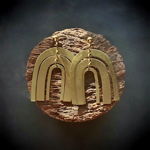 May include: A pair of gold-toned earrings with a layered arch design. The earrings are made of metal and have a polished finish.
