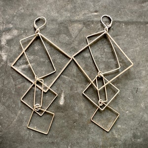 May include: A pair of silver geometric earrings with multiple interlocking square shapes.