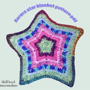 Może przedstawiać: Kolorowy, w kształcie gwiazdy koc szydełkowy w odcieniach różu, fioletu, niebieskiego i zielonego. Koc zawiera tekst "Aurora star blanket pattern pdf" i "Skill level-intermediate". Koc jest przedmiotem ręcznie robionym.