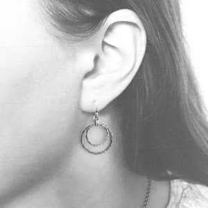 Puede incluir: Pendientes de plata de doble c&iacute;rculo con textura martillada. Los pendientes cuelgan de la oreja de una persona.