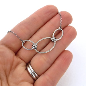 May include: A silver necklace with three interconnected oval links. The links are connected by twisted wire.