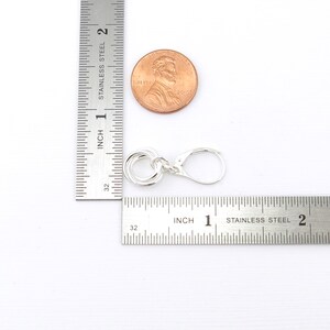 May include: A silver-colored earring with a lever back clasp. The earring features a design of four interlocking circles. A penny is next to the earring for size comparison. The earring is approximately 0.75 inches in length.