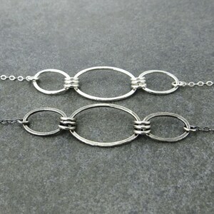 May include: Two silver chain necklaces with oval-shaped links. The links are connected by smaller, round links. The necklaces are on a gray background.