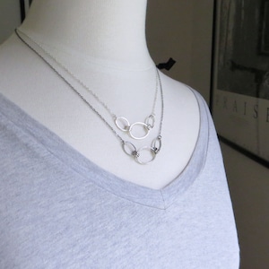 May include: A silver necklace with multiple interconnected oval rings. The necklace is layered on a mannequin wearing a gray t-shirt.