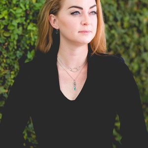 May include: A woman wearing a black velvet top with a silver chain necklace and a silver pendant with a turquoise stone.