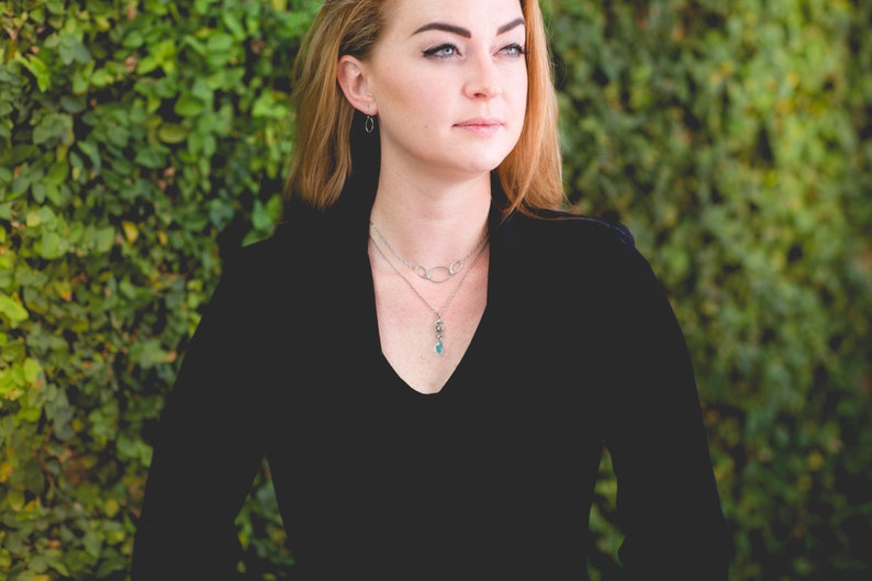 May include: A woman wearing a black velvet top with a silver chain necklace and a silver pendant with a turquoise stone.