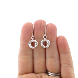 May include: A pair of silver-colored dangle earrings. Each earring features a cluster of interconnected rings, suspended from a simple hook. The earrings are displayed against a white background.