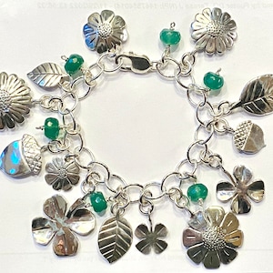 May include: A silver charm bracelet with green gemstone beads and charms shaped like leaves, flowers, and acorns.