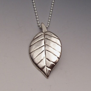 May include: A silver leaf pendant necklace with a detailed vein pattern. The pendant is attached to a silver chain.