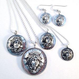 May include: A set of four silver necklaces with coin pendants featuring the profile of a woman's face. The necklaces are of varying lengths and the coins are of different sizes. The coins are dated 1918, 1954, and 1992. There are also a pair of matching silver earrings with coin pendants featuring the same woman's face.