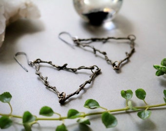 May include: A pair of bronze earrings shaped like a triangle made of delicate twig-like branches.