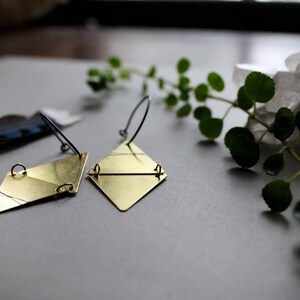 May include: A pair of gold geometric earrings with a diamond shape. The earrings are made of brass and have a simple, minimalist design.