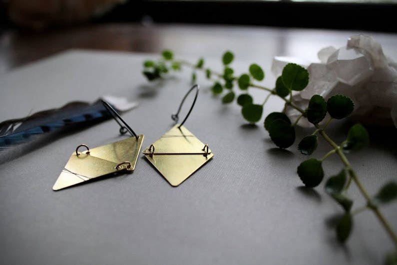 May include: A pair of gold geometric earrings with a diamond shape. The earrings are made of brass and have a simple, minimalist design.