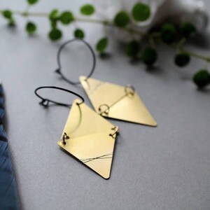 May include: A pair of gold-toned geometric earrings with a diamond shape. The earrings are suspended from thin black hoops.