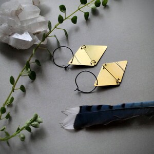 May include: A pair of gold geometric earrings with a diamond shape. The earrings are made of brass and have a simple, modern design.