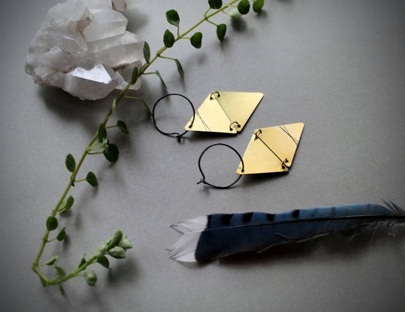 May include: A pair of gold geometric earrings with a diamond shape. The earrings are made of brass and have a simple, modern design.