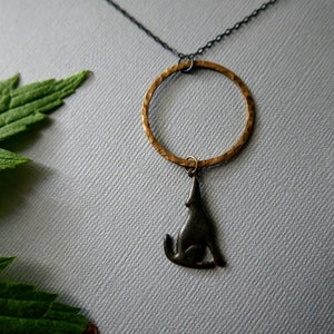 May include: A silver wolf pendant hangs from a hammered gold circle on a black chain. The pendant and circle are both textured.