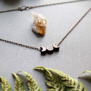 May include: A copper chain necklace with a three-phase moon pendant. The pendant is made of dark wood and has a matte finish.