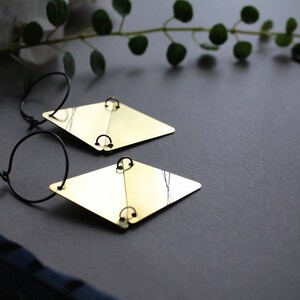 May include: A pair of gold-toned earrings with black hoops and diamond-shaped pendants. The earrings are on a gray surface.
